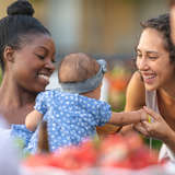 People of different races sharing a meal, smiling at baby